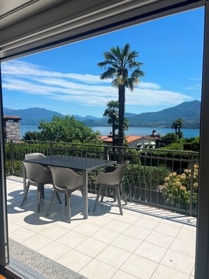 Un balcon avec une table et des chaises, une vue sur un lac, des montagnes et un palmier.