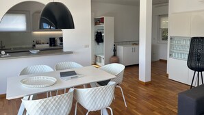 A modern kitchen with white cabinetry, a dining area with a white table and chairs, and a black fan.