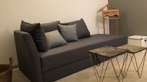 A dark grey sofa with multiple cushions, a small wooden hanger, and a small table with metal legs.