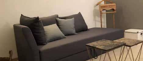 Ein dunkelgraues Sofa mit vielen Kissen, ein kleiner Holzhaken und ein Tisch mit Metallbeinen.