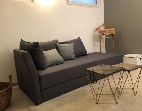 Un canapé gris foncé agrémenté de plusieurs coussins, un petit porte-manteau en bois et une petite table aux pieds en métal.