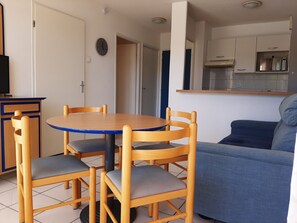 Un espacio habitable compacto con una mesa redonda de madera y cuatro sillas, un sofá, una kitchenette y un televisor sobre un mueble.