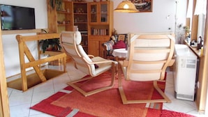 Un soggiorno con televisione, sedie di legno, una libreria e un quadro appeso al muro.