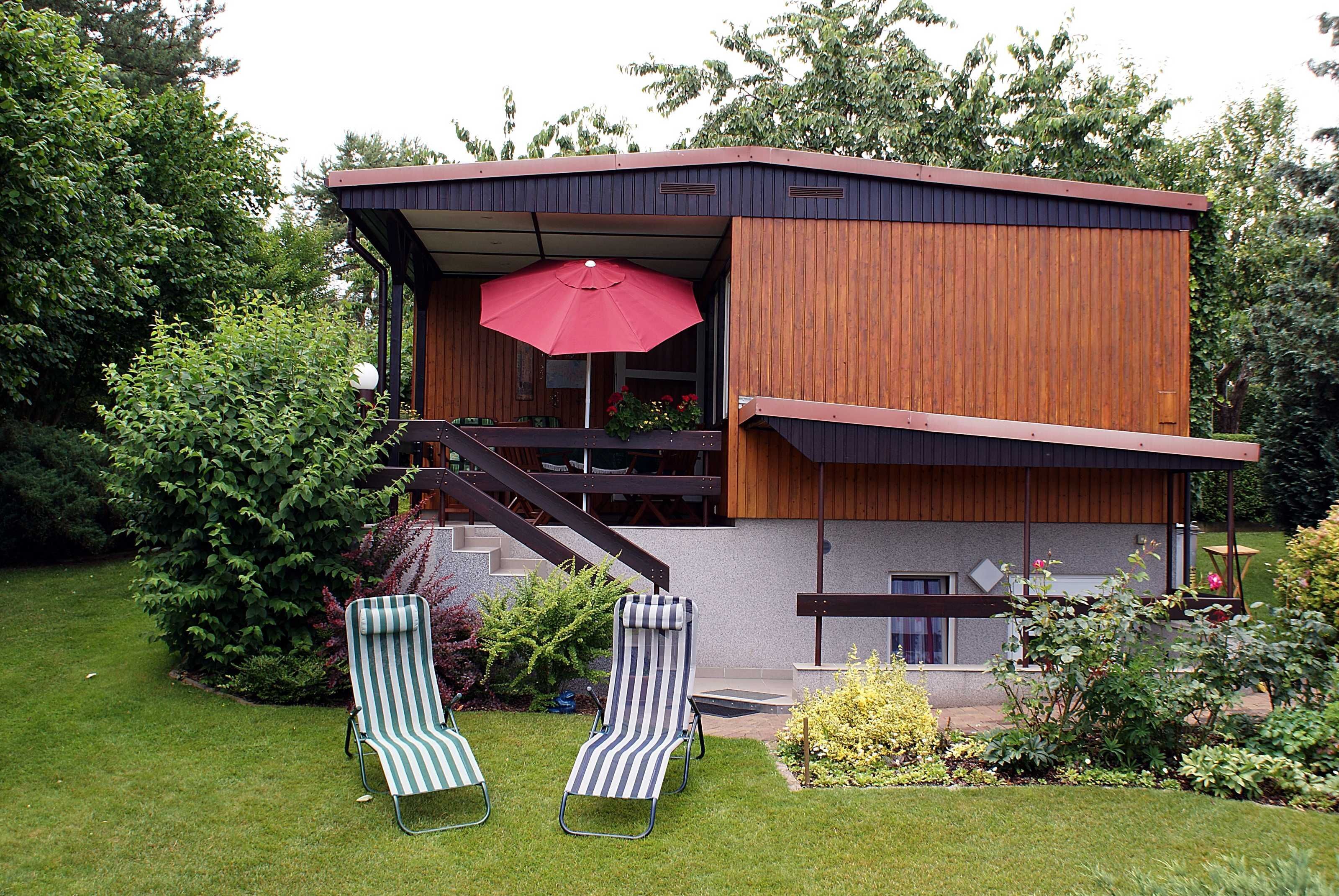 A modern house with a wooden exterior, a balcony, and two striped lounge chairs.