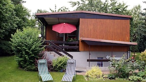 Una casa moderna con facciata in legno, un balcone e due poltrone da relax a righe.