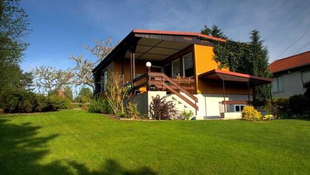 Una casa moderna con una terrazza in legno, una scala e un prato curato.