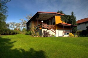 A modern house with a wooden deck, a staircase, and a well-maintained lawn.