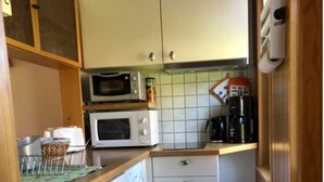 Una cucina compatta con mobili bianchi, un forno a microonde, un tostapane e una macchina per il caffè.