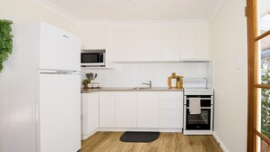 Une cuisine compacte avec des meubles blancs, un four à micro-ondes, une cuisinière et un petit évier.