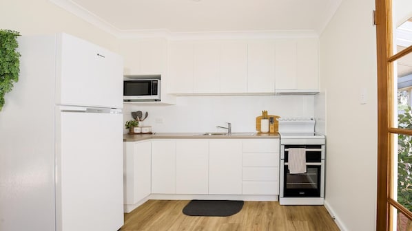 Una cocina compacta con armarios blancos, un microondas, una estufa y un lavamanos pequeño.