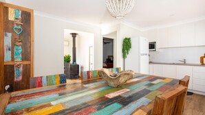 Une cuisine moderne avec des meubles blancs, une table à manger en bois aux plateaux colorés et un cœur décoratif sur la porte.