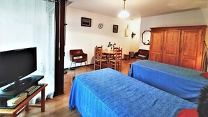 A room with a TV, two beds, a dining table with chairs, and a wooden cabinet. - Bright and functional studio ideally located in Aix-les-Bains (Aix-les-Bains)