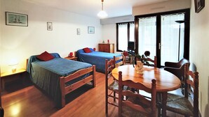 A room with two single beds, a wooden dining table with chairs, a television, and a window with curtains. - Bright and functional studio ideally located in Aix-les-Bains (Aix-les-Bains)