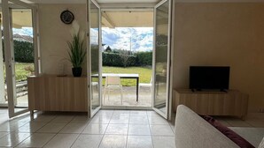 A spacious living room with a sliding glass door leading to a patio, a television on a wooden stand, and a potted plant.