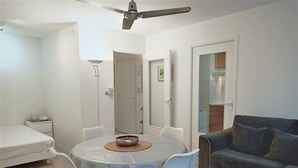 Un salon moderne avec une table de salle à manger ronde, des chaises blanches, un canapé gris et un ventilateur de plafond.