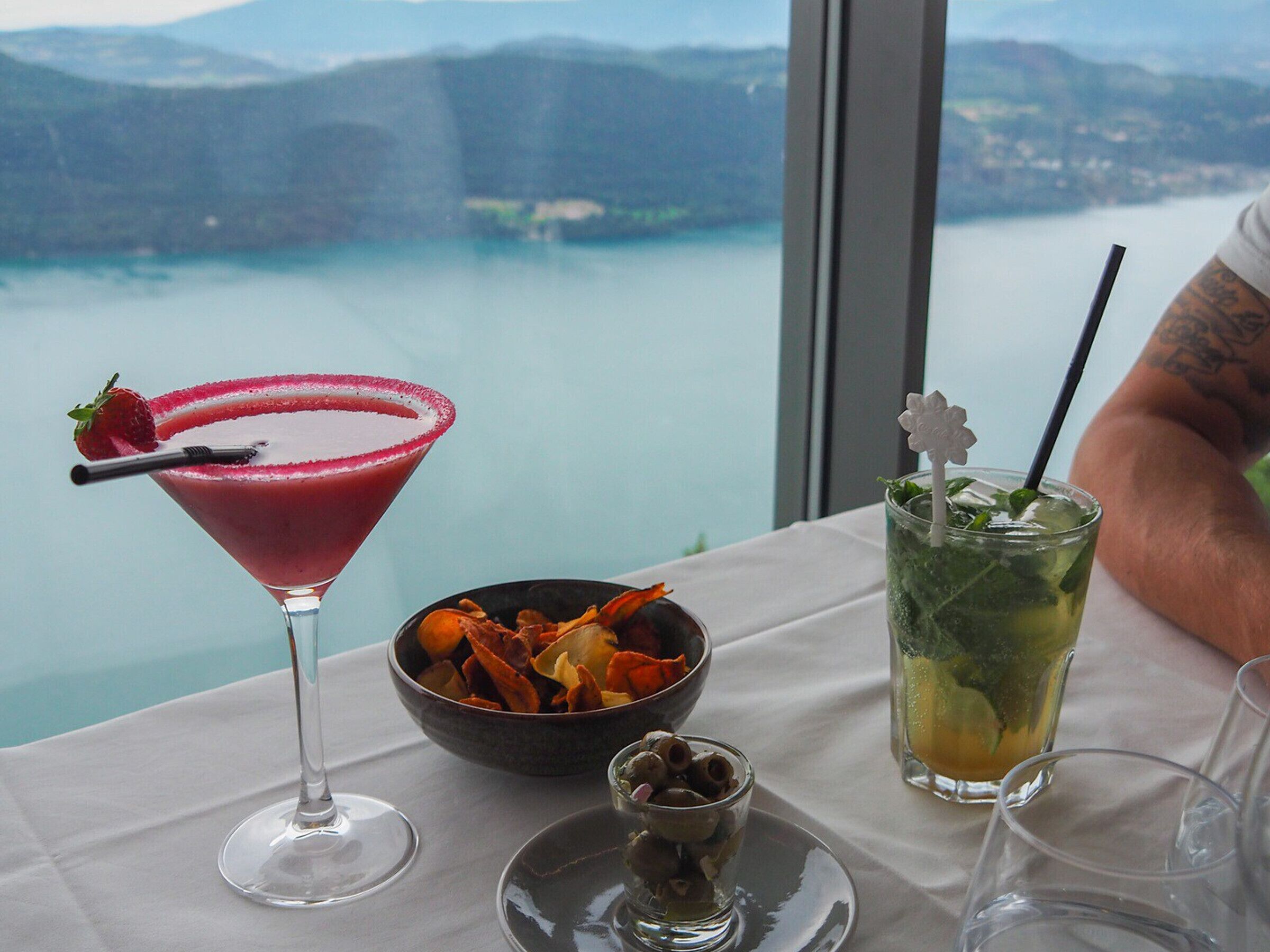 A table with a martini glass, a bowl of snacks, a glass of iced drink, and a wine glass.