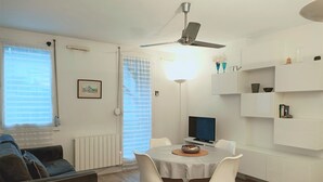 Un salon moderne comprenant un coin repas, un ventilateur de plafond, un téléviseur et une bibliothèque.