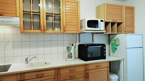 Une cuisine avec des meubles de rangement en bois, un évier blanc, un four à micro-ondes, un grille-pain et un réfrigérateur.