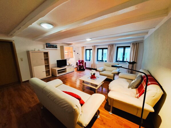 Ein Wohnzimmer mit einer Couch, Sesseln, einem Fernseher und einem Couchtisch.