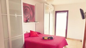 A bedroom with a bed, a red bedspread, a red pillow, a small shelf with a decorative item, a white door, and a white ceiling light. - PRIVATE GARDEN & HEATED POOL, WIFI Fiber 600Mb / s Total comfort and total privacy (La Oliva)