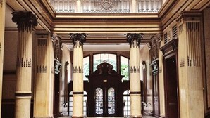 Een statig portaal met hoge zuilen, een zwart-wit schaakbordvloer en een centrale, gewelfde deuropening.