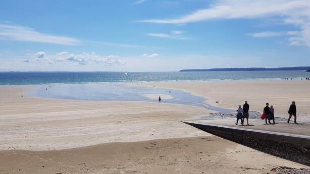 Ein Strand mit einer Steinmauer und Menschen, die darauf entlanggehen.