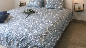 A bed with a patterned bedspread, two pillows, a wall-mounted artwork, and two bedside lamps. - In De Duinen (Middelkerke)