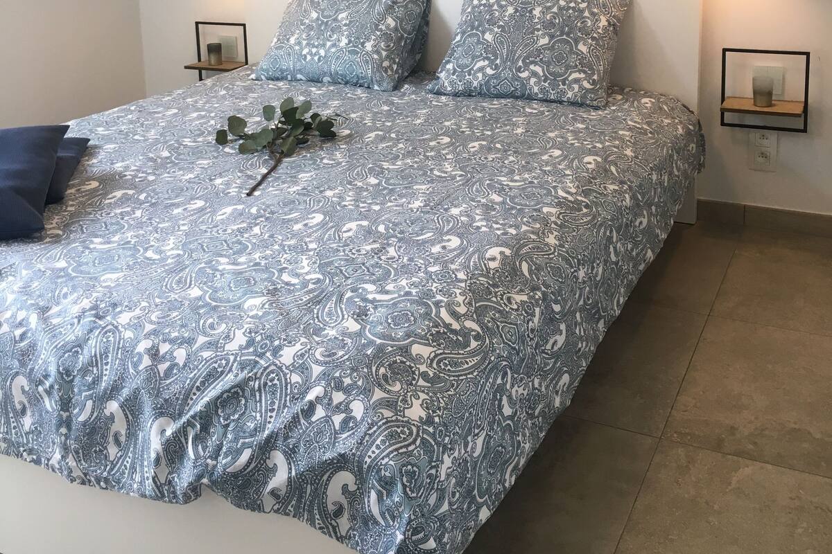 Ein Bett mit einem gemusterten Überwurf, zwei Kissen, einem Wandbild und zwei Nachttischlampen.