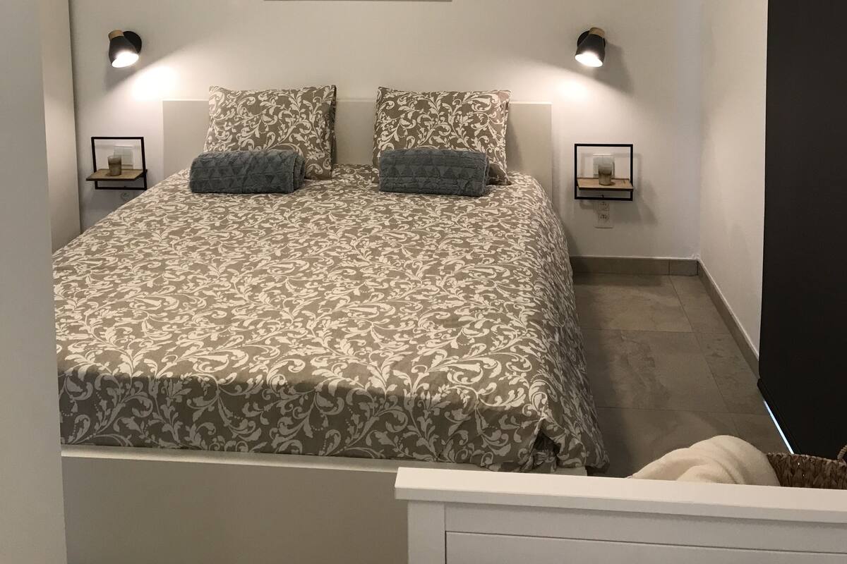 Ein Schlafzimmer mit einem Bett, zwei Nachttischen, einem Wandbild und einer Deckenleuchte.