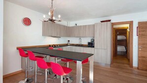 Una cocina moderna con una isla central, taburetes rojos, una araña y un reloj en la pared.