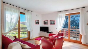 Una sala de estar con un sofá rojo, un televisor y piso de madera. Hay tres cuadros en la pared.