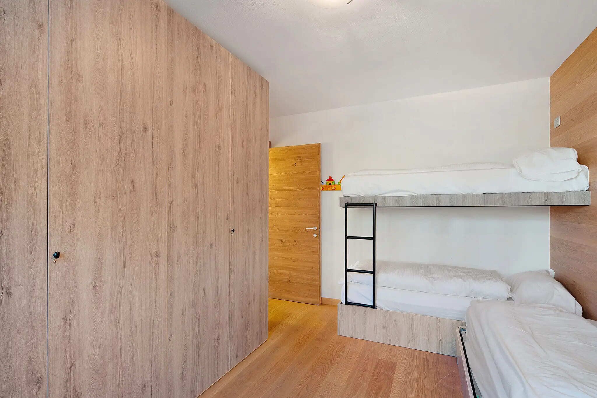 Une petite pièce avec un lit superposé, une armoire en bois et une petite porte en bois.