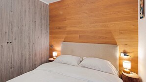Un dormitorio con cabecera de madera, cama con ropa blanca, dos lámparas de noche y una mesita de noche.