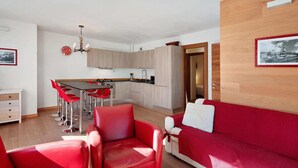 Una sala de estar moderna con muebles rojos, una cocina con armarios de madera clara y una zona de comedor con sillas rojas.