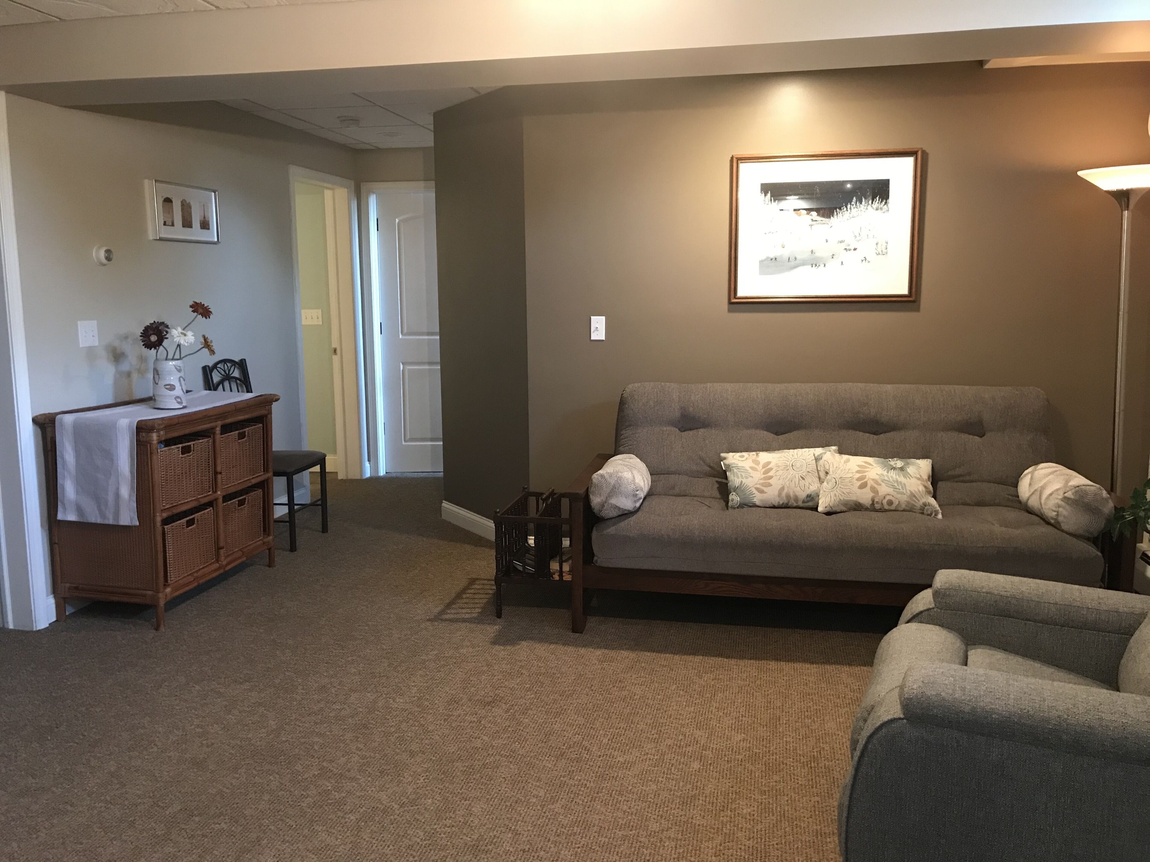 A living room with a grey sofa, a small table, wicker baskets, and a framed picture on the wall.