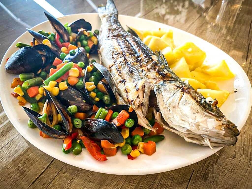 A plate of grilled fish, mussels, and mixed vegetables.