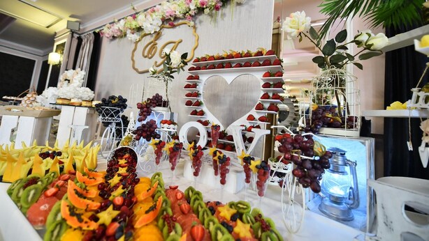 A fruit and cheese board with a decorative heart-shaped centerpiece and a floral arrangement above. - Hotel Nevada (Constanta)