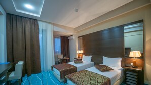 A hotel room with two beds, a desk, a chair, a desk lamp, and an air conditioning unit. - Hotel Nevada (Constanta)