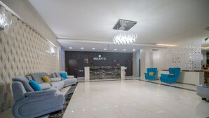 A modern hotel lobby with a reception desk labeled "RECEPTION," a marble floor, and blue and gray seating areas. - Hotel Nevada (Constanta)