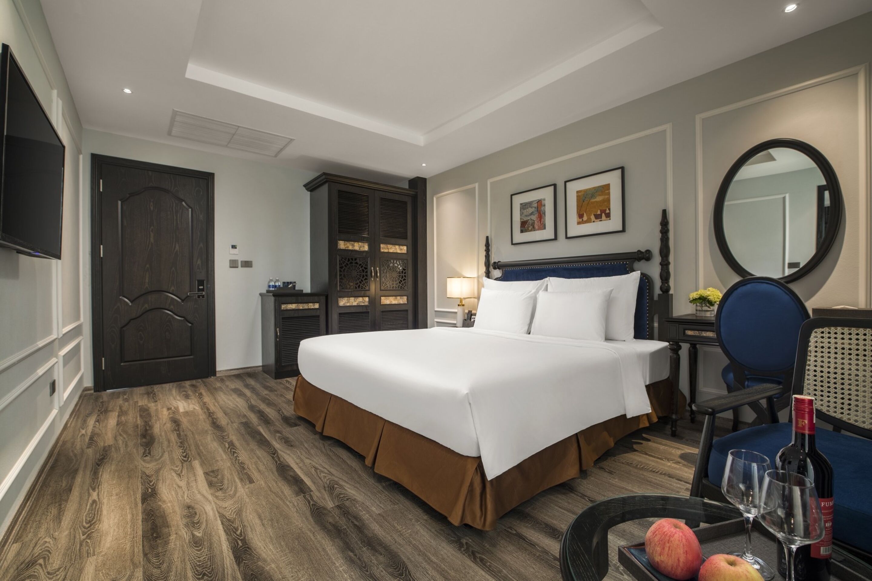 A hotel room with a large bed, a desk with a chair, a wardrobe, a television, and a mirror.