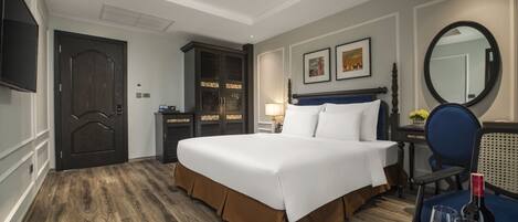 A hotel room with a large bed, a desk with a chair, a wardrobe, a television, and a mirror.