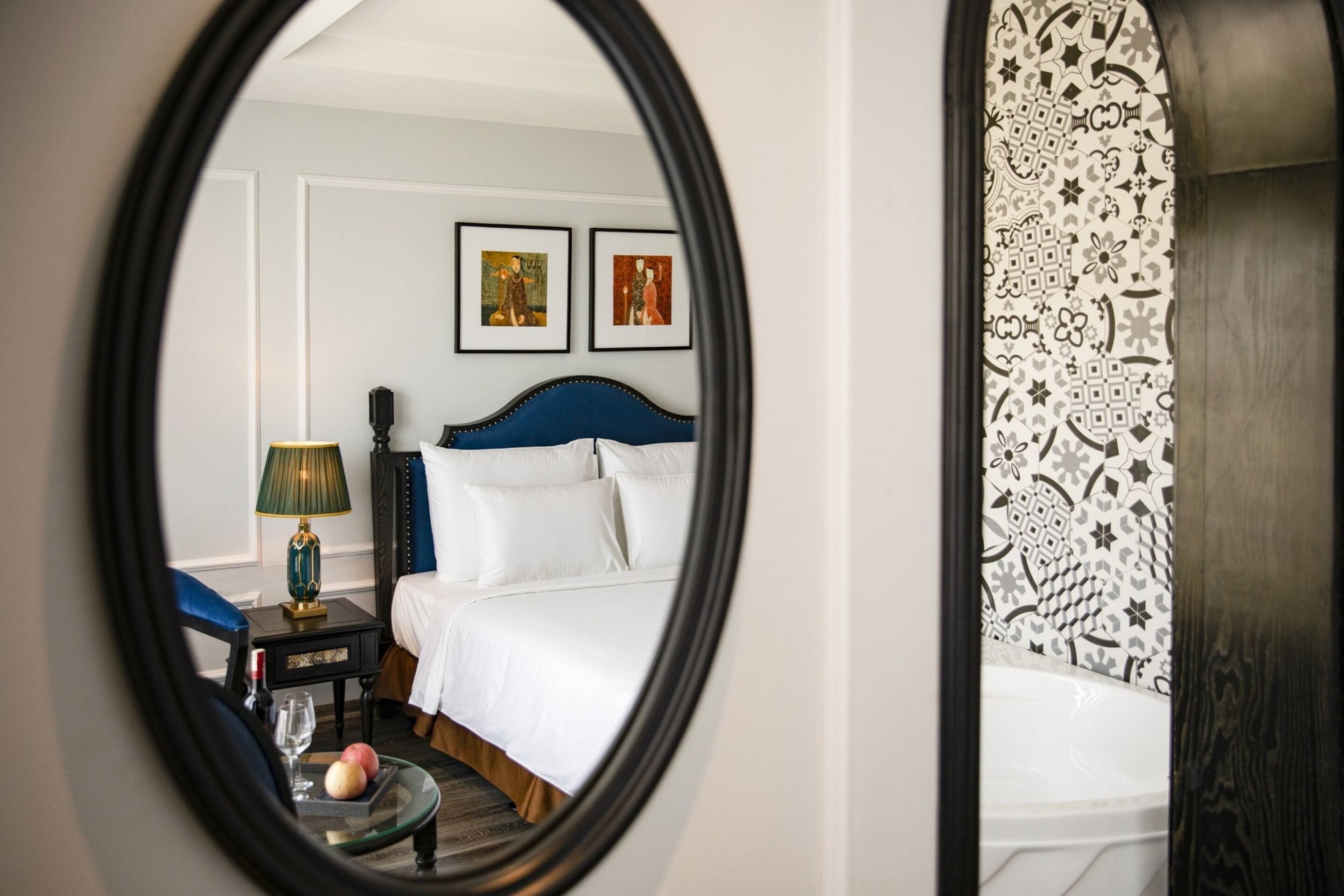 A bedroom with a bed, a nightstand, a lamp, and a mirror reflecting the room.