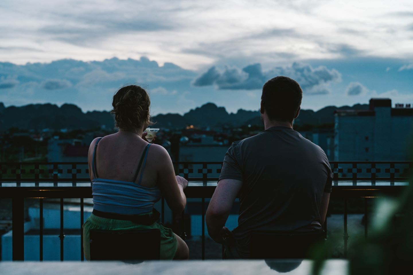 Deux personnes sont assises sur un balcon, d’où elles peuvent admirer une vue sur la ville, avec des montagnes en arrière-plan.