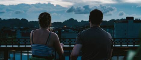 Deux personnes sont assises sur un balcon, d’où elles peuvent admirer une vue sur la ville, avec des montagnes en arrière-plan.