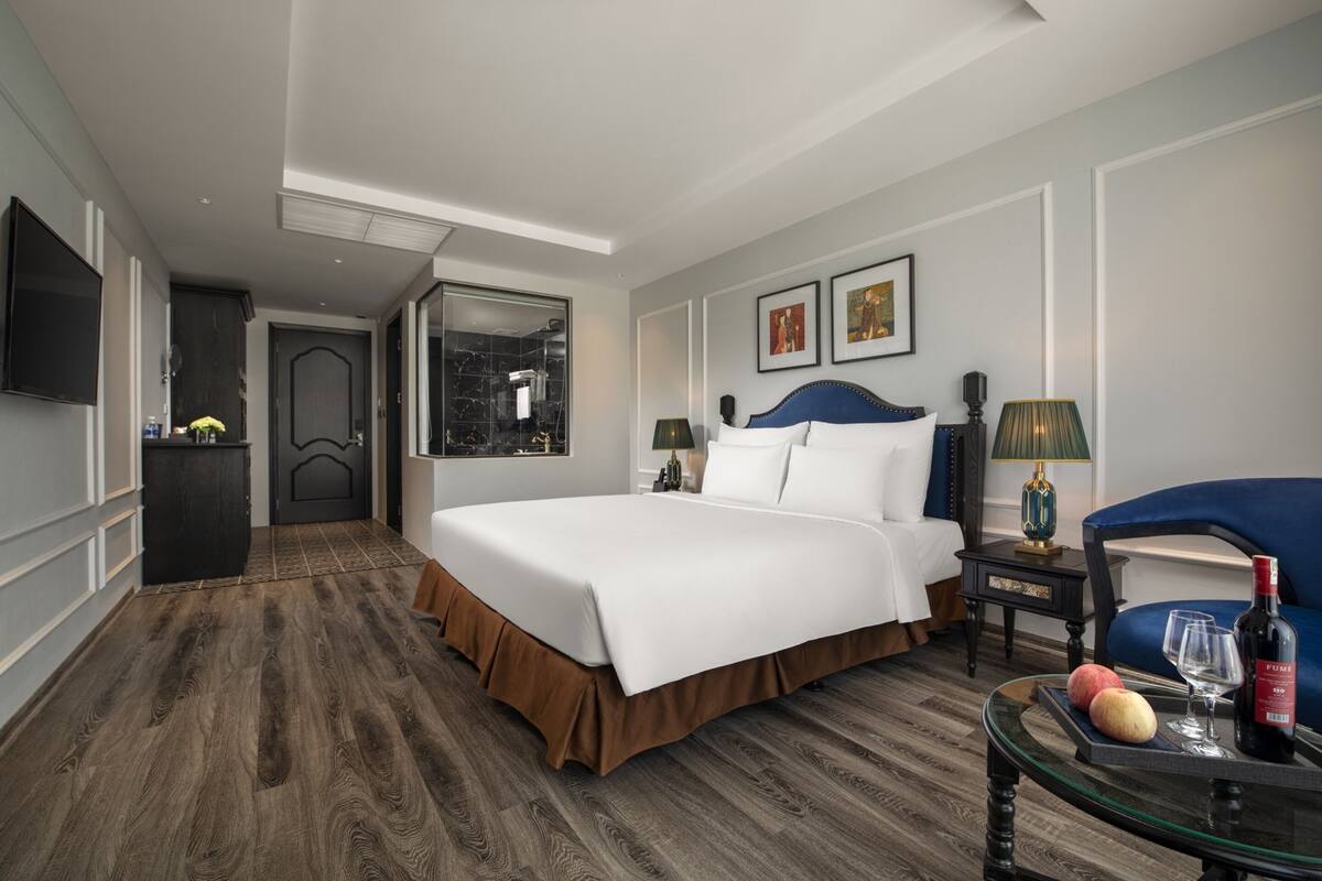 A hotel room with a large bed, a TV, a desk with a lamp, and a chair.