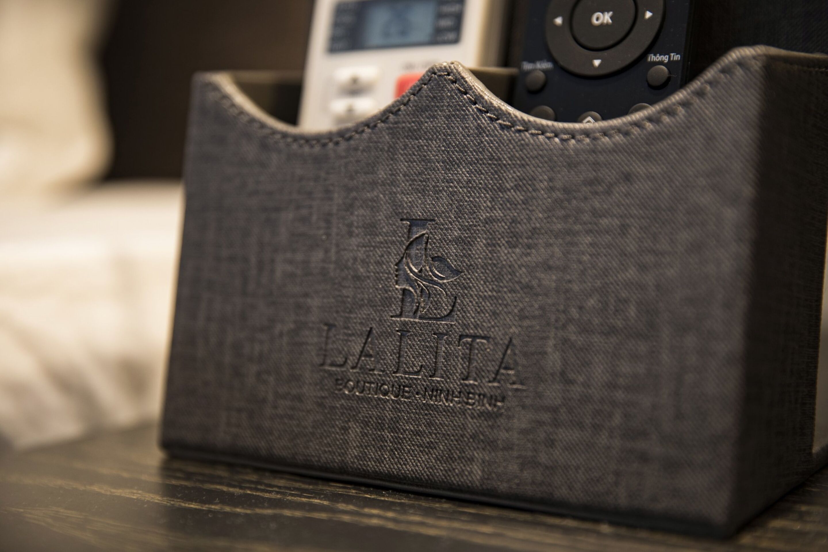 Une coque en tissu à texture sombre, ornée de motifs en relief et d’un logo, posée sur une surface en bois.