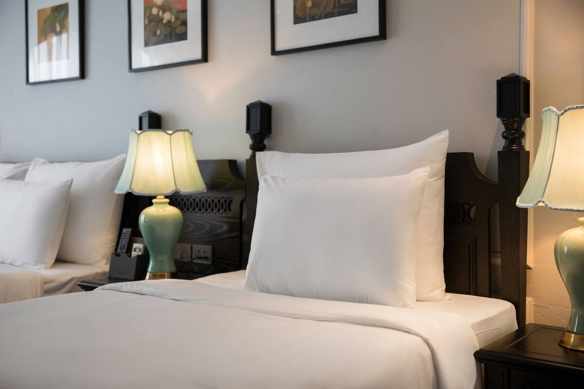 A hotel room with two beds, each with white linens and a single lamp.