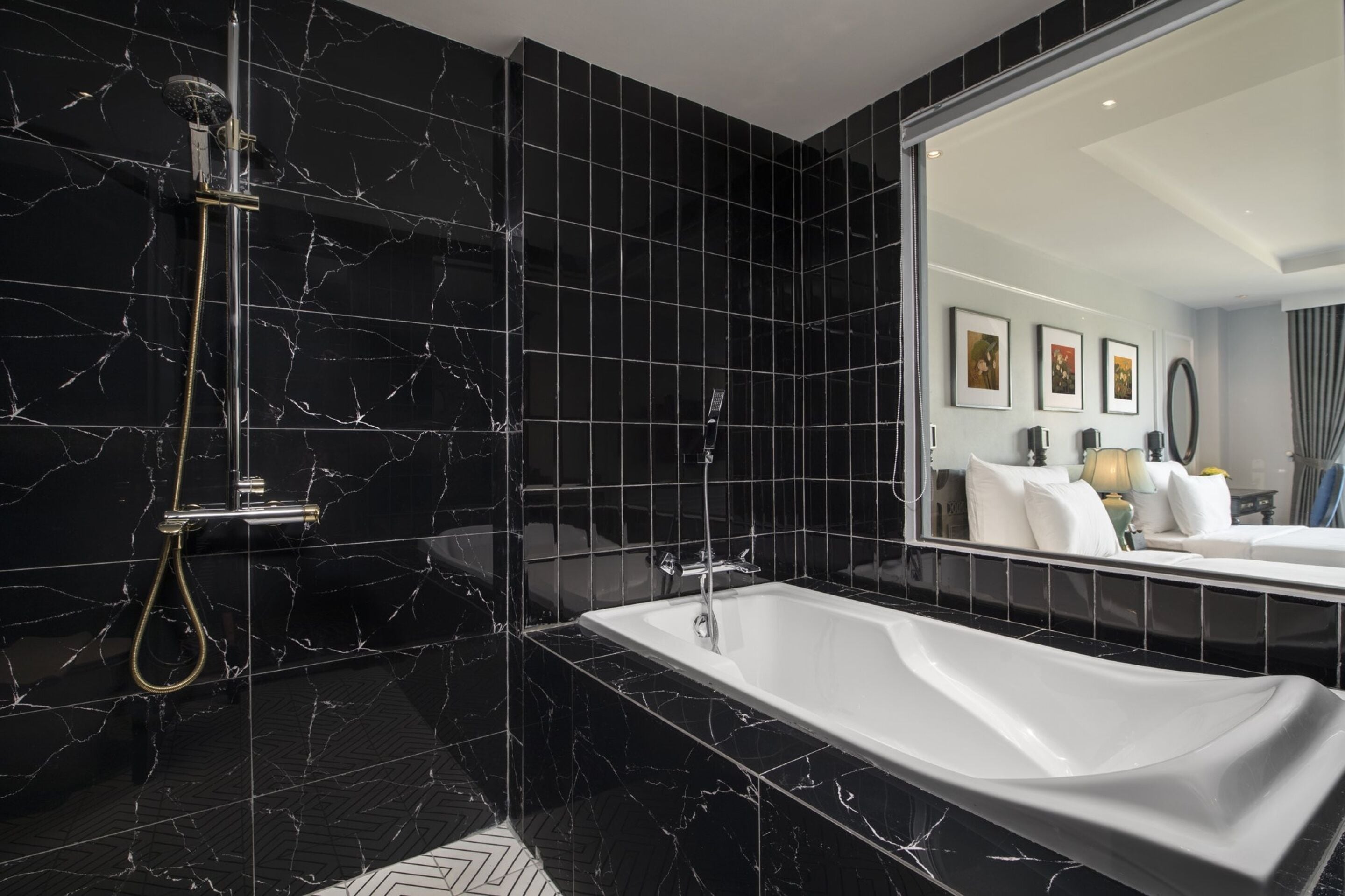Un baño moderno con azulejos de mármol negro, una bañera independiente y un espejo grande que refleja el ambiente.