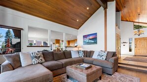 A spacious living area with a large sectional sofa, a small ottoman, and a patterned rug. - Dynamic Views, Hot Tub, Gym, 2nd Living Room, Garage and More. (Carnelian Bay)