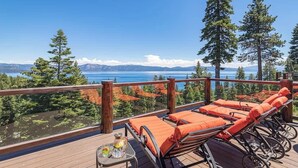 A deck with lounge chairs and a table, overlooking a lake and mountains. - Dynamic Views, Hot Tub, Gym, 2nd Living Room, Garage and More. (Carnelian Bay)
